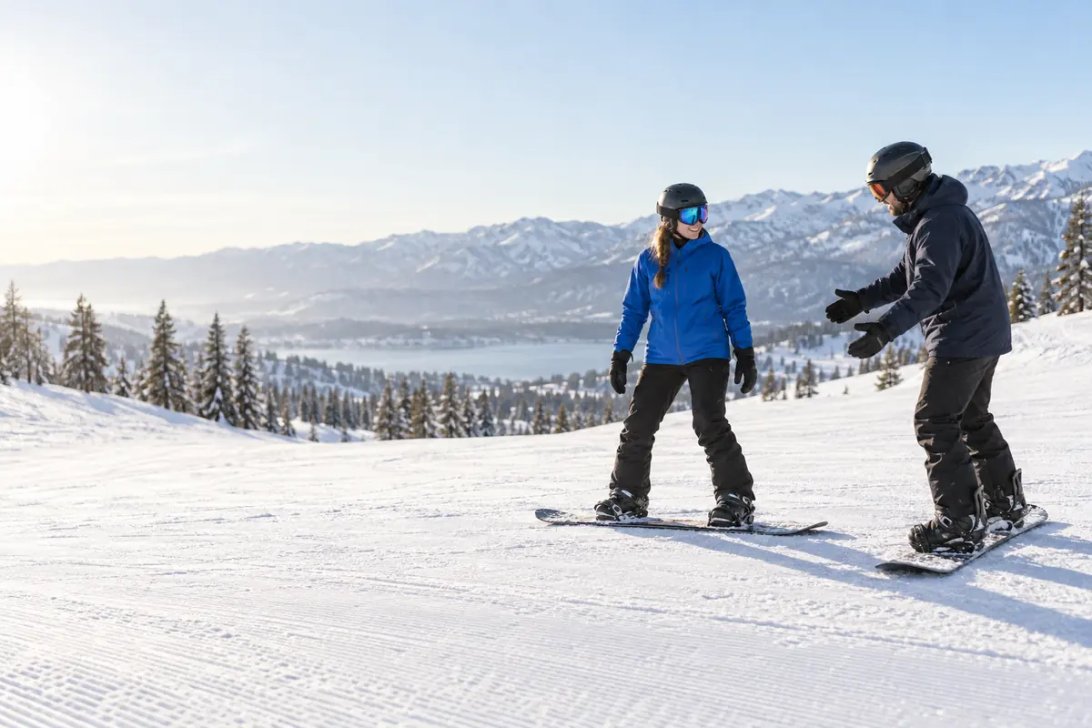 Instructor and beginner on a groomed slope during a snowboard lesson