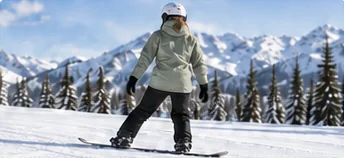 Snowboarder in a pale jacket and white helmet standing on a groomed slope before practicing how to ride switch on a snowboard