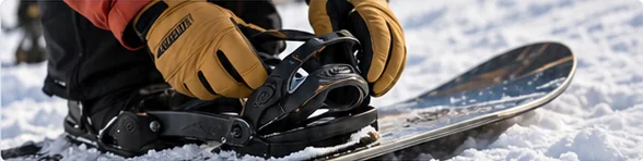 Gloved hands fastening a strap on a snowboard binding while setting up snowboard bindings