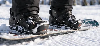 Snowboarder fastening binding straps to strap into a snowboard on the snow